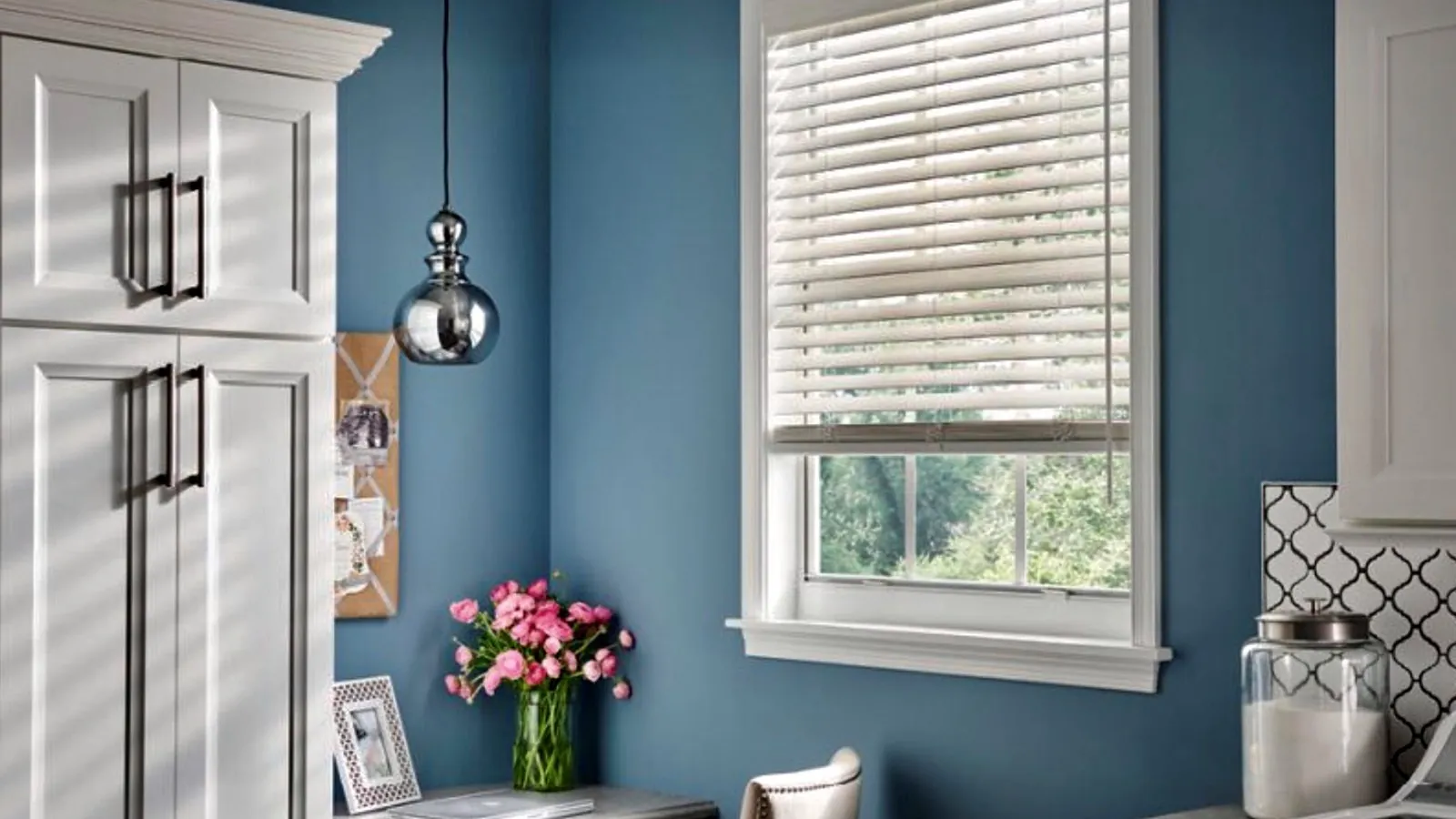 White horizontal blinds in a blue kitchen with a pendant light, installed by Harbor View Blinds